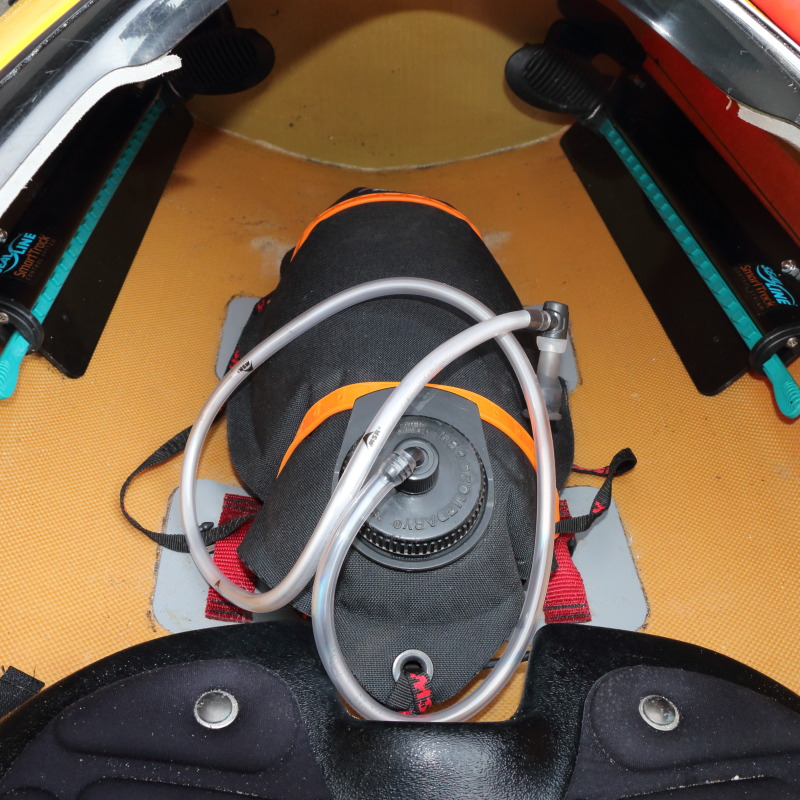 a waterbag with drinking hose strapped to the floor of a kayak's cockpit