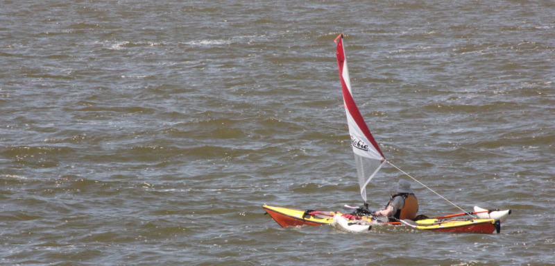 A single sea kayak equipped with a Hobie sail and amas.