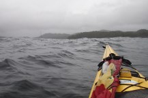 View from the kayak: the tip of a sailboat mast barely visible beyond a swell