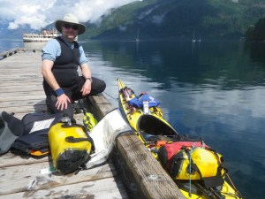 a kayaker kneels on the dock beside his boat