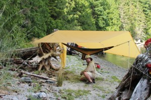 a camper kneels next to his tarped hammock
