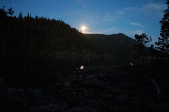 the moon rises behind rocky hills