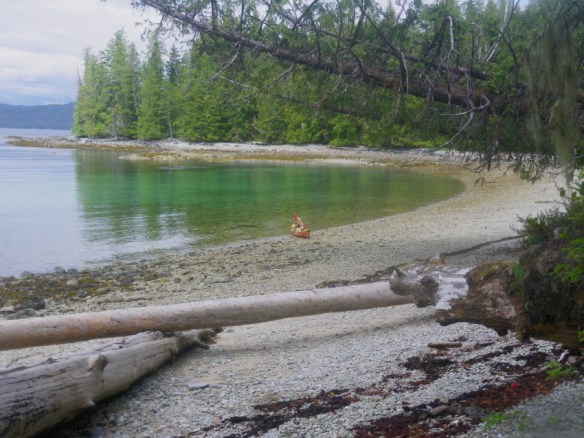 a sea kayak pulled up on the beach in a sheltered bay