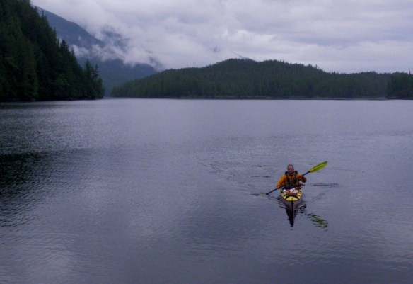 a kayaker paddles across a calm and cloudy inlet