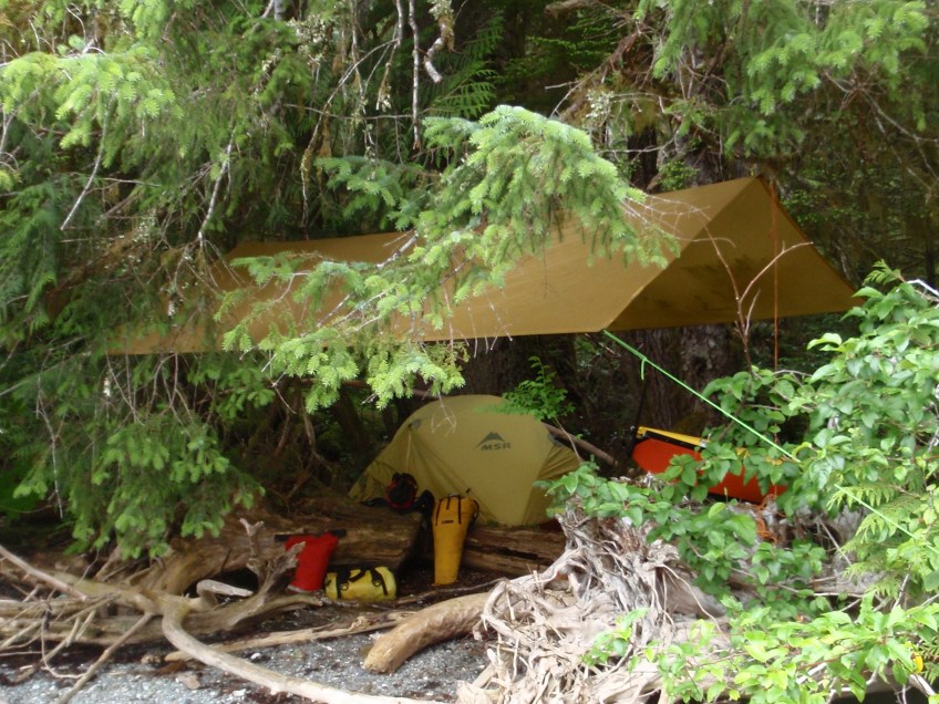 a tarp and a tent rigged on a stony beach