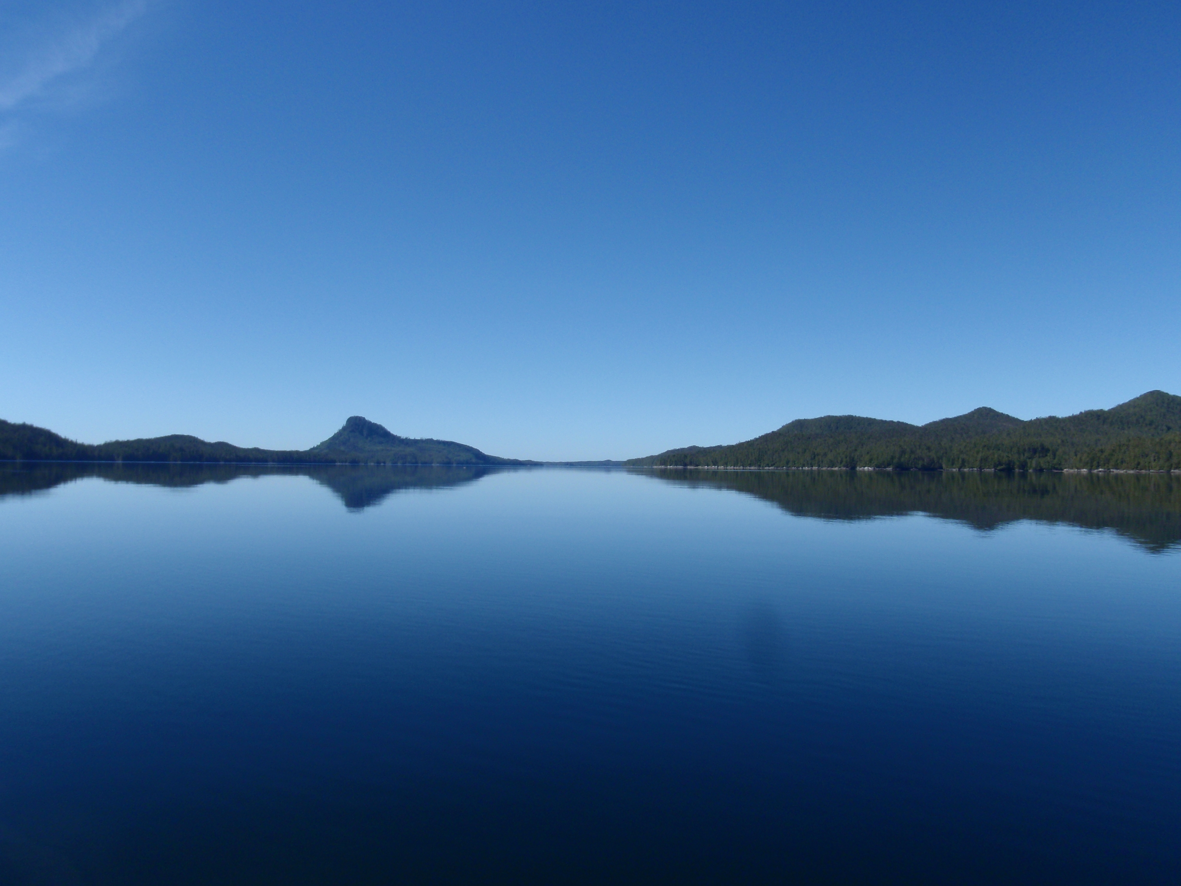 A calm sea reflects the land and a blue sky