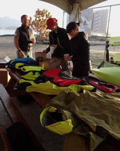 paddlers admire a table of sea kayak clothing and equipment