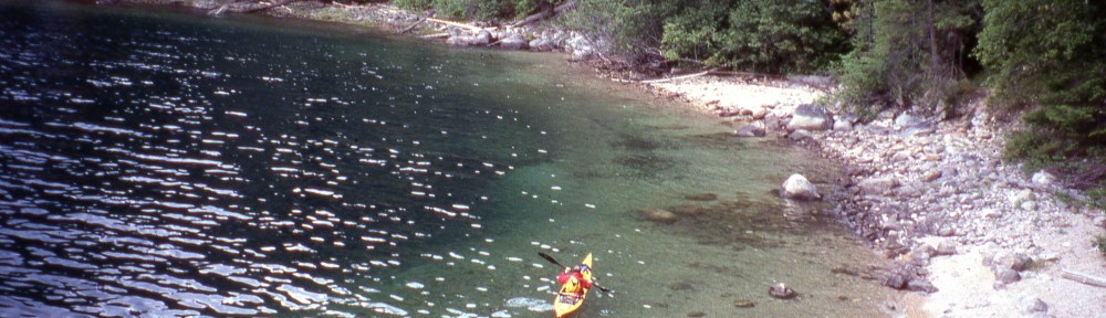 a kayaker paddles near the shore of Slocan Lake