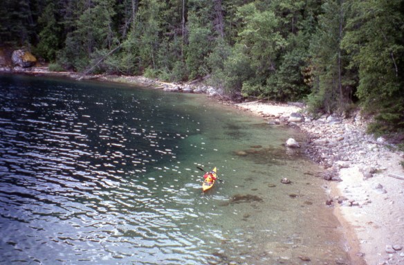a kayaker paddles near the shore of Slocan Lake
