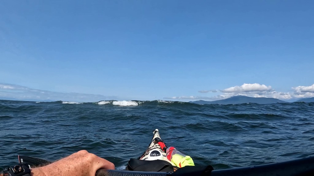 a sea kayaker's point of view of a breaking swell near the bow of the boat
