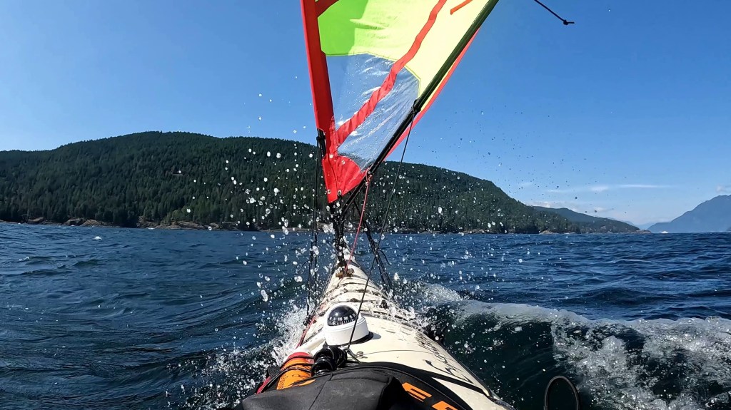 a wave breaks across the bow of a sea kayak sailing